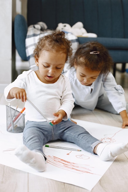 Free photo two africanamerican girls drawing on a floor. toddler and her older sister drowing on a paper