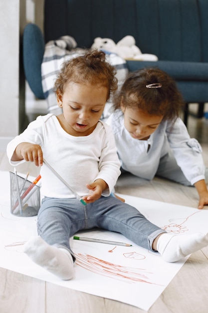 Two africanamerican girls drawing on a floor. Toddler and her older sister drowing on a paper