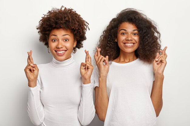 두 명의 아프리카 계 미국인 여학생이 손가락을 교차하고 행운을 믿고 시험에서 우수한 점수를 받고 행복하게 미소지었습니다.