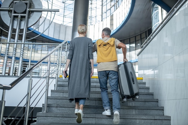 Two airline passengers with travel documents and baggage going upstairs