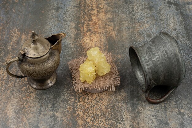 Two ancient kettles with slices of sweet sugar on marble surface. 