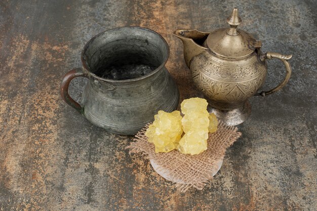 Two ancient kettles with slices of sweet sugar on marble surface. 