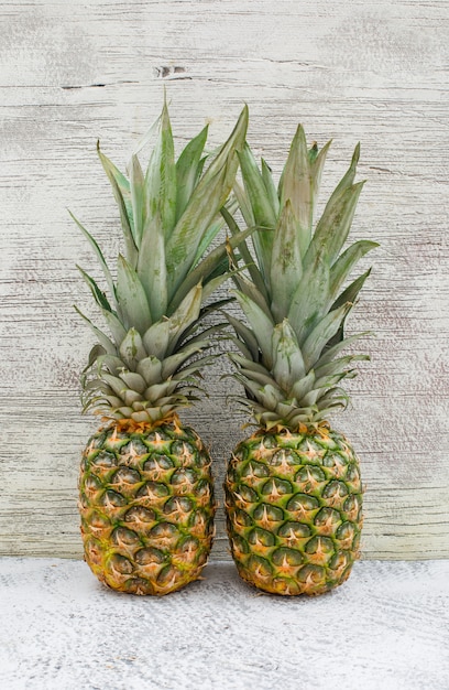 Two aromatic pineapples on grey wall and grungy, side view.