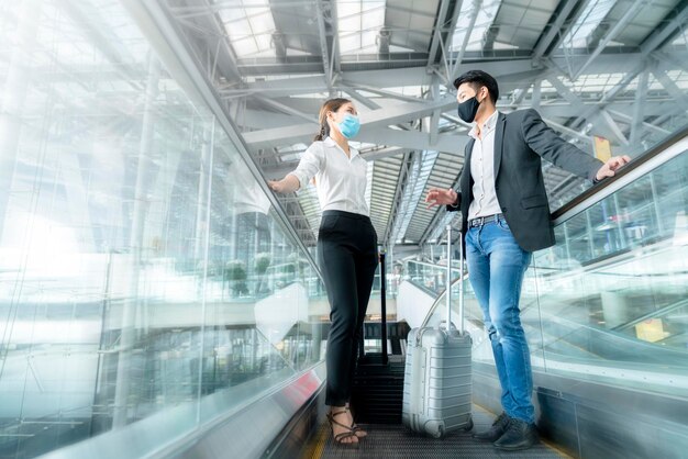 Two asian business partners with face mask protection social distancing new normal lifestyle Business travellers walking in airport with luggage motion movement