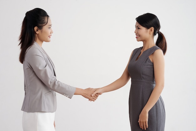 Two Asian business women standing indoors, shaking hands and smiling