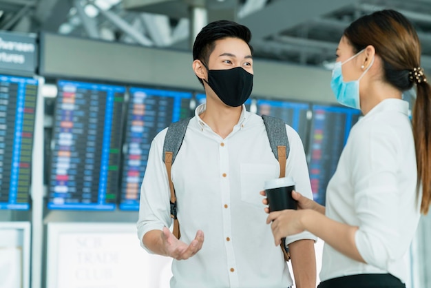 Due uomini d'affari asiatici e una donna d'affari con protezione della maschera facciale nella conversazione del terminal dell'aeroporto internazionale vicino al concetto di business del bordo informativo