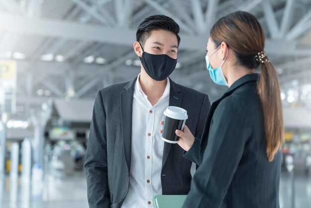 Два азиатских бизнесмена и деловая женщина с защитной маской для лица в международном терминале аэропорта, встреча с планшетом возле скамейки для воды, новая нормальная концепция туристического бизнеса
