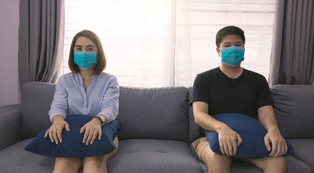 2​人​の​アジア人​カップル​の​恋人​が​、​コロナ​ウイルス​covid​-​19​による​ウイルス​の​流行​の​新種​で​、​社会的​距離​の​概念​から​離れて​自宅​の​ソファ​に​座っています​。