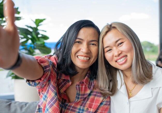 Two asian friends taking selfies on mobile phone in coffee shop.