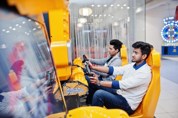 Two asian guys compete on speed rider arcade game racing simulator machine