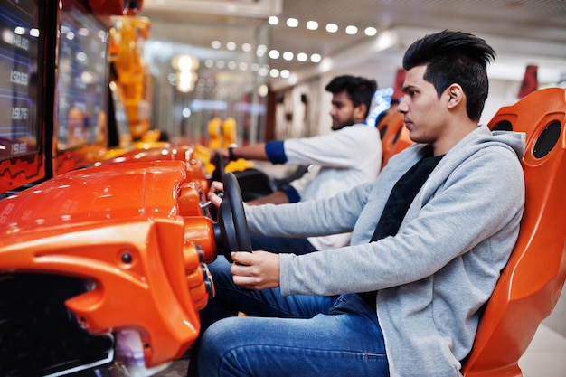 Two asian guys compete on speed rider arcade game racing simulator machine