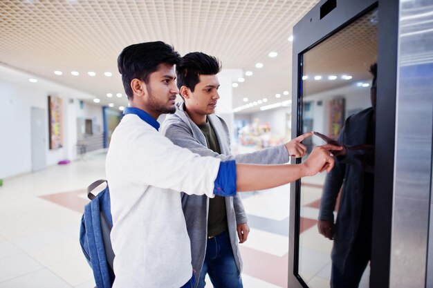 Two asian guys touching screen of electronic information desk in mall