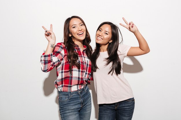 Two asian pretty cheerful ladies sisters showing peace gesture.