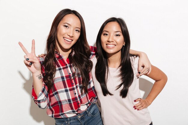 Two asian pretty cheerful ladies sisters showing peace gesture.