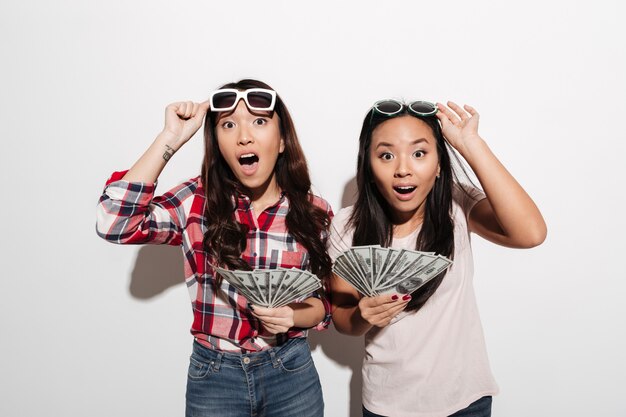 Two asian pretty shocked cute ladies holding money.