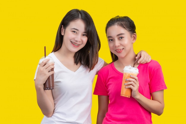 2 азиатских женщины выпивая замороженный чай молока и замороженное какао на желтом цвете.