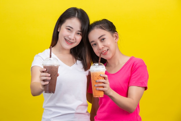 アジアの2人の女性がアイスミルクティーと黄色のアイスココアを飲んでいます。