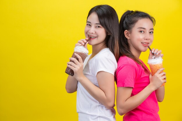 Two Asian women drinking iced milk tea and iced cocoa on a yellow .