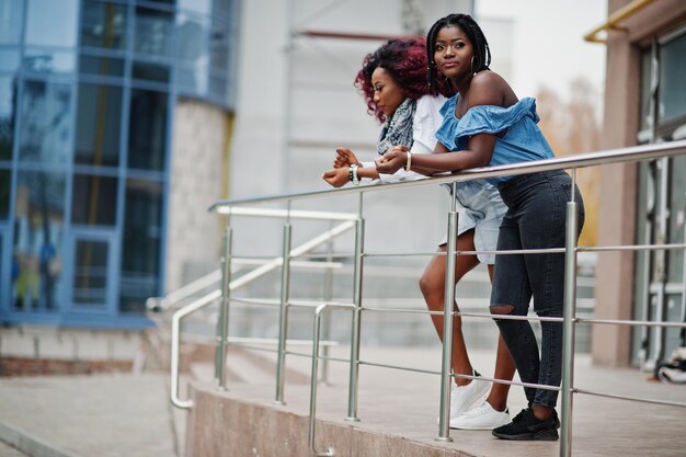 Two attractive african american womans posed near railings against modern multistory building