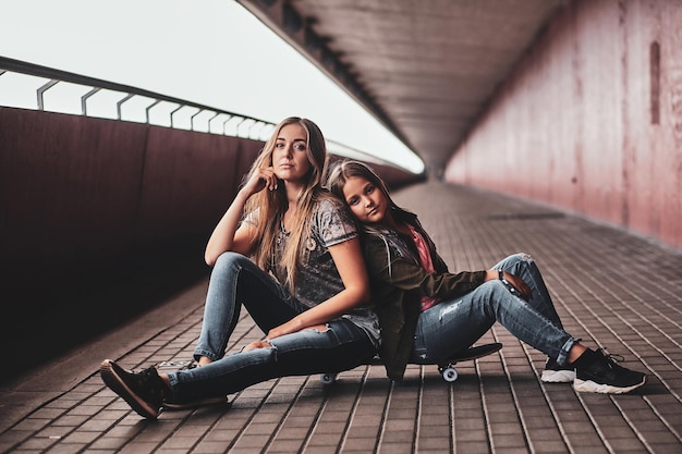 Two attractive friendly teenagers are sitting on the skateboard in long tunnel.