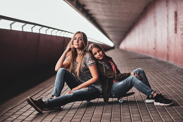 Два привлекательных дружелюбных подростка сидят на скейтборде в длинном туннеле.