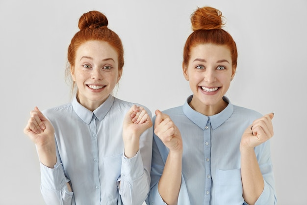 Two attractive happy young redhead women with hair knots wearing light-blue shirts