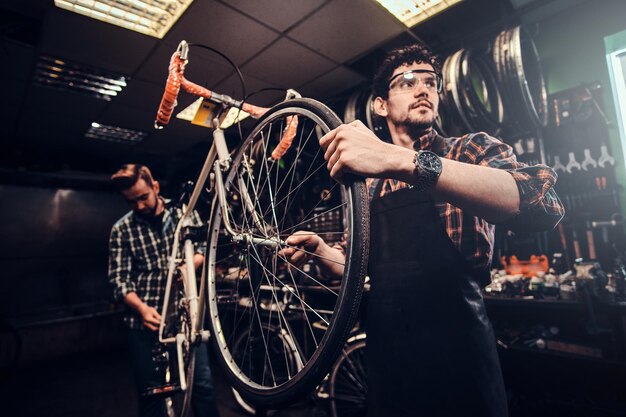 Два привлекательных мужчины работают над починкой велосипеда в оживленной мастерской.