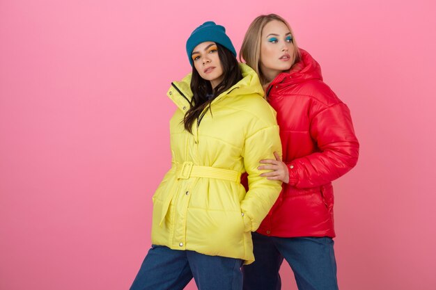 빨간색과 노란색 색상의 화려한 겨울 다운 재킷, 따뜻한 옷 패션 트렌드에 분홍색 배경에 포즈 두 매력적인 세련된 여성