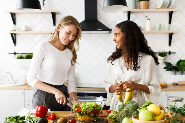 Two attractive women on the kitchen are cooking healthy breakfast from fruits and vegetables