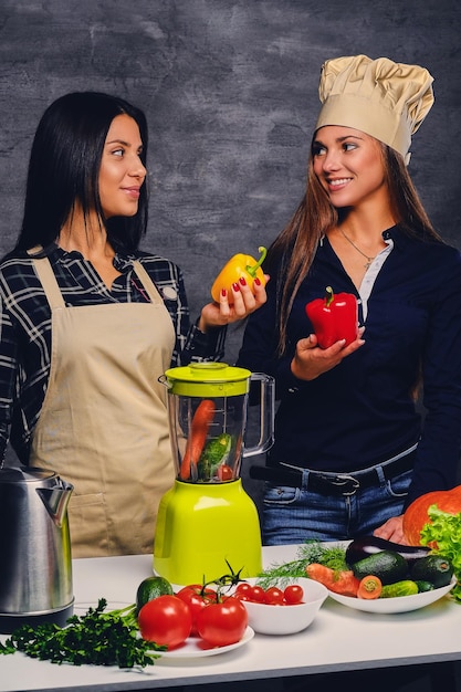 Two attractive young women preparing vegan vegetable juice with blender.