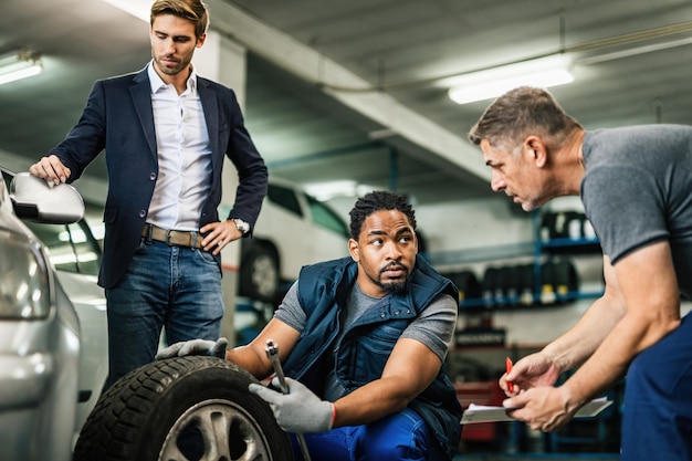 Foto gratuita due meccanici automatici che collaborano durante la riparazione del pneumatico dell'auto del cliente presso l'officina di riparazione auto