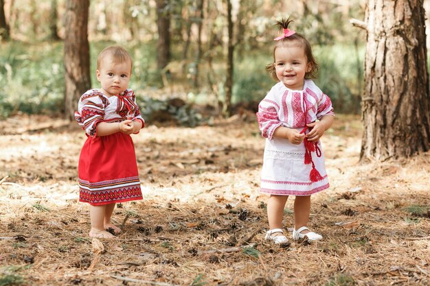 Two baby girls in traditional ukrainian dresses playing in spring forest.
