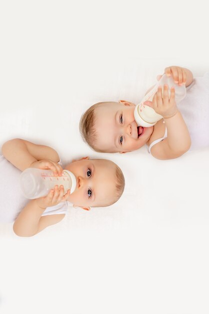 Premium Photo Two Babies Suck Milk From A Bottle Lying In A Crib In The Children S Room On A White Bed