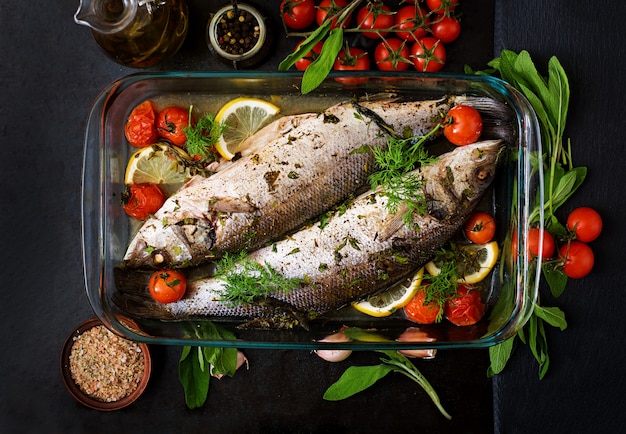 Two baked seabass in a baking dish with spices on an black table. Top view