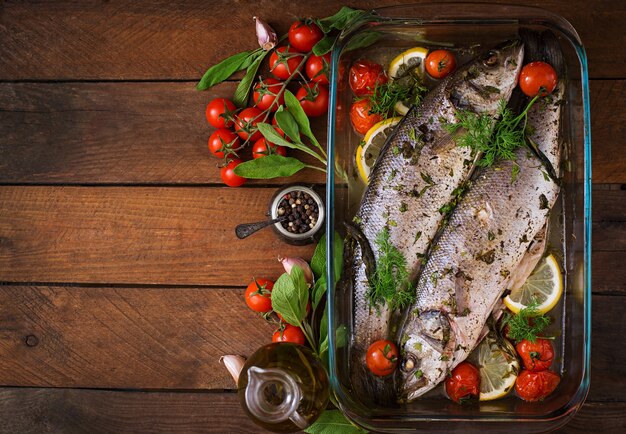 Two baked seabass in a baking dish with spices on an wooden table. Top view