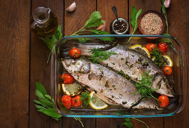 Two baked seabass in a baking dish with spices on an wooden table. Top view