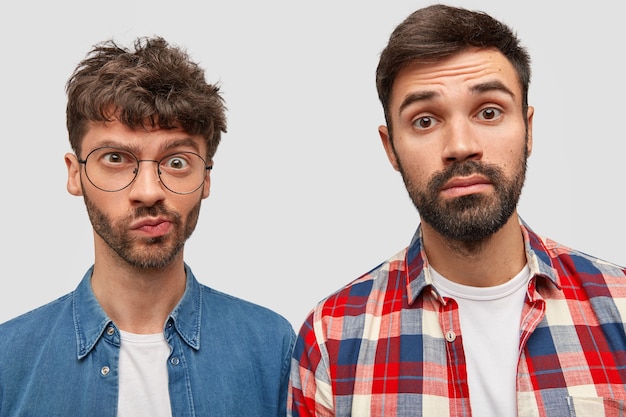 Two bearded man journalists have puzzled expressions, work on creating article, look at camera with bewilderment, dressed in fashionable shirts