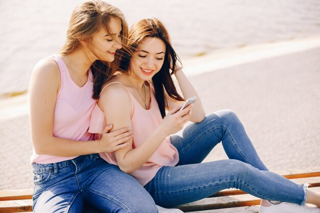 two beautiful and bright friends in pink t-shirts and blue jeans sitting in the sunny city 