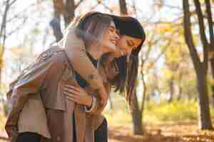 Foto gratuita due belle amiche che trascorrono del tempo insieme. due giovani sorelle sorridenti che camminano nel parco d'autunno e si abbracciano. ragazze brune e bionde che indossano cappotti.