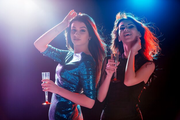 Two beautiful girls dancing at the party drinking champagne