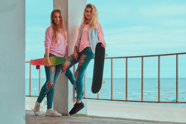 2人の美しい姉妹は、スケートボードを持って海辺の近くで素敵な夏の日を楽しんでいます。