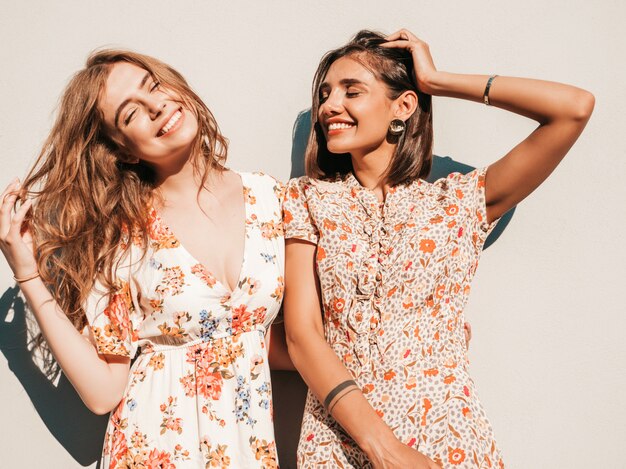 Two beautiful smiling girls in trendy summer sundress posing on the street