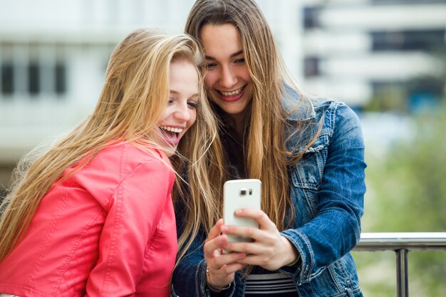 Two beautiful students using mobile phone in the street.