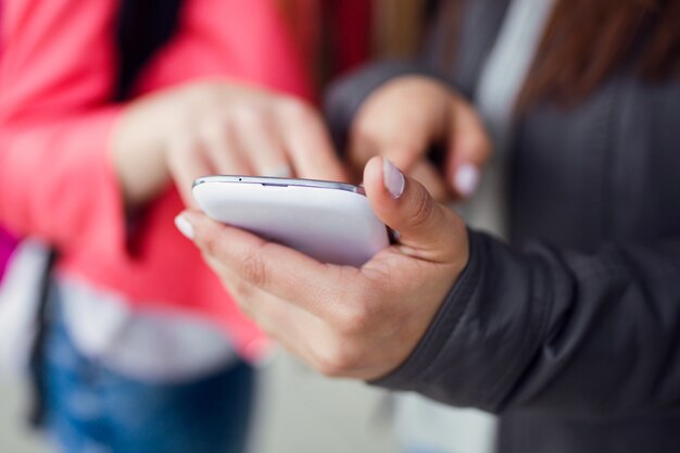 Two beautiful students using mobile phone in the street.