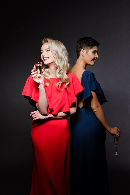 Two beautiful women in evening dresses smiling, holding champaign glass