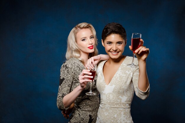 Two beautiful women in evening dresses smiling, holding wine glasses