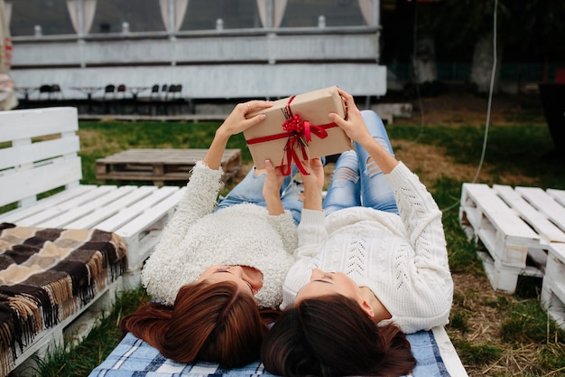 Free photo two beautiful women lie on the bench and unpacks a gift