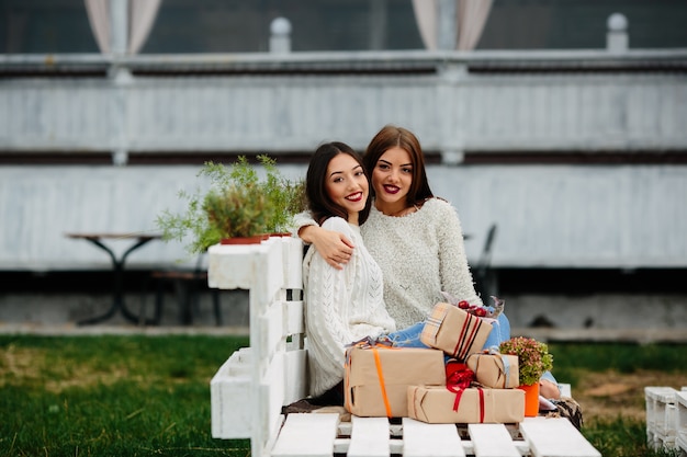Two beautiful women sitting on a bench, holding gifts in their hands and looking
