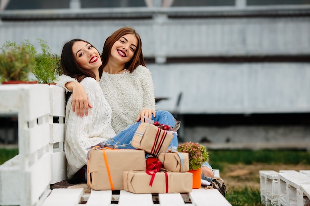 Two beautiful women sitting on a bench, holding gifts in their hands and looking