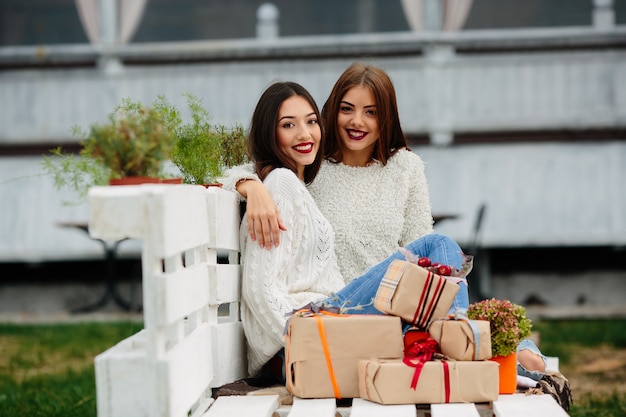 Two beautiful women sitting on a bench, holding gifts in their hands and looking